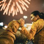Woman Sitting and Patting Dog with Fireworks behind
